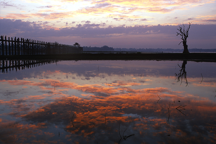Tagesanbruch an der alten U Bein-Brücke nahe Amarapura. Seitdem der Taungthaman-See aufgestaut ist, spiegeln sich die Wolken in ihm das ganze Jahr über.
